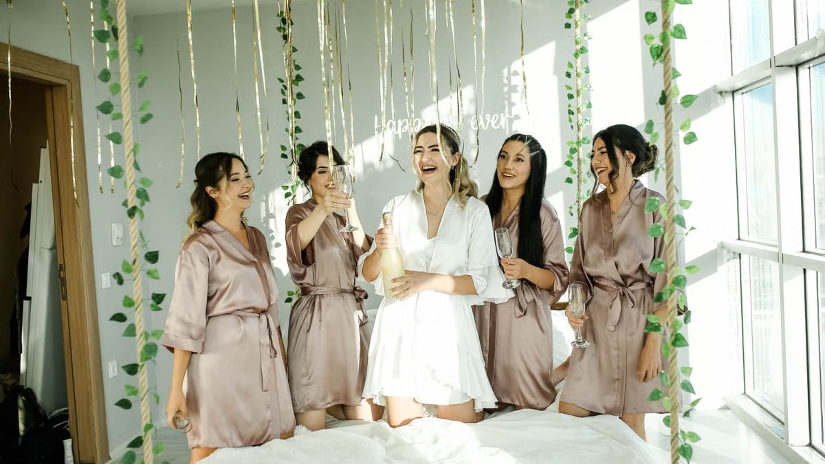 Bride and bridesmaids celebrating with champagne indoors. Joyful wedding preparation moment.